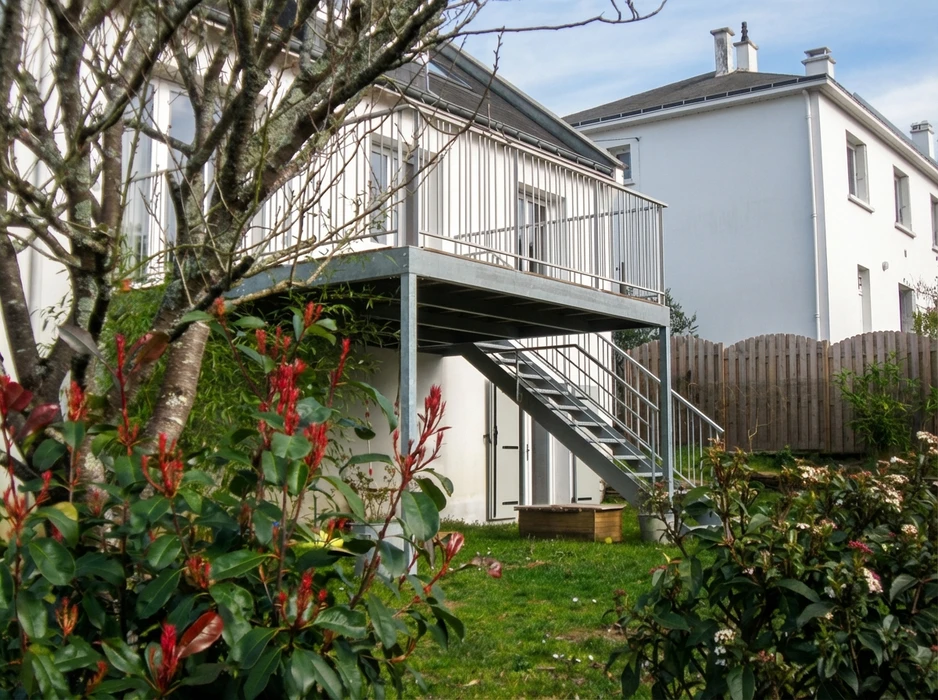 Terrasse en porte-à-faux sur structure métallique galvanisée, accessible par escalier droit à marches caillebotis avec garde-corps tubulaire