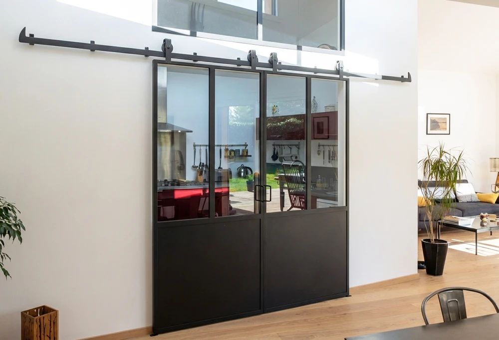 Couloir intérieur moderne avec verrière atelier à cadres métalliques noirs donnant sur un hall d'entrée
